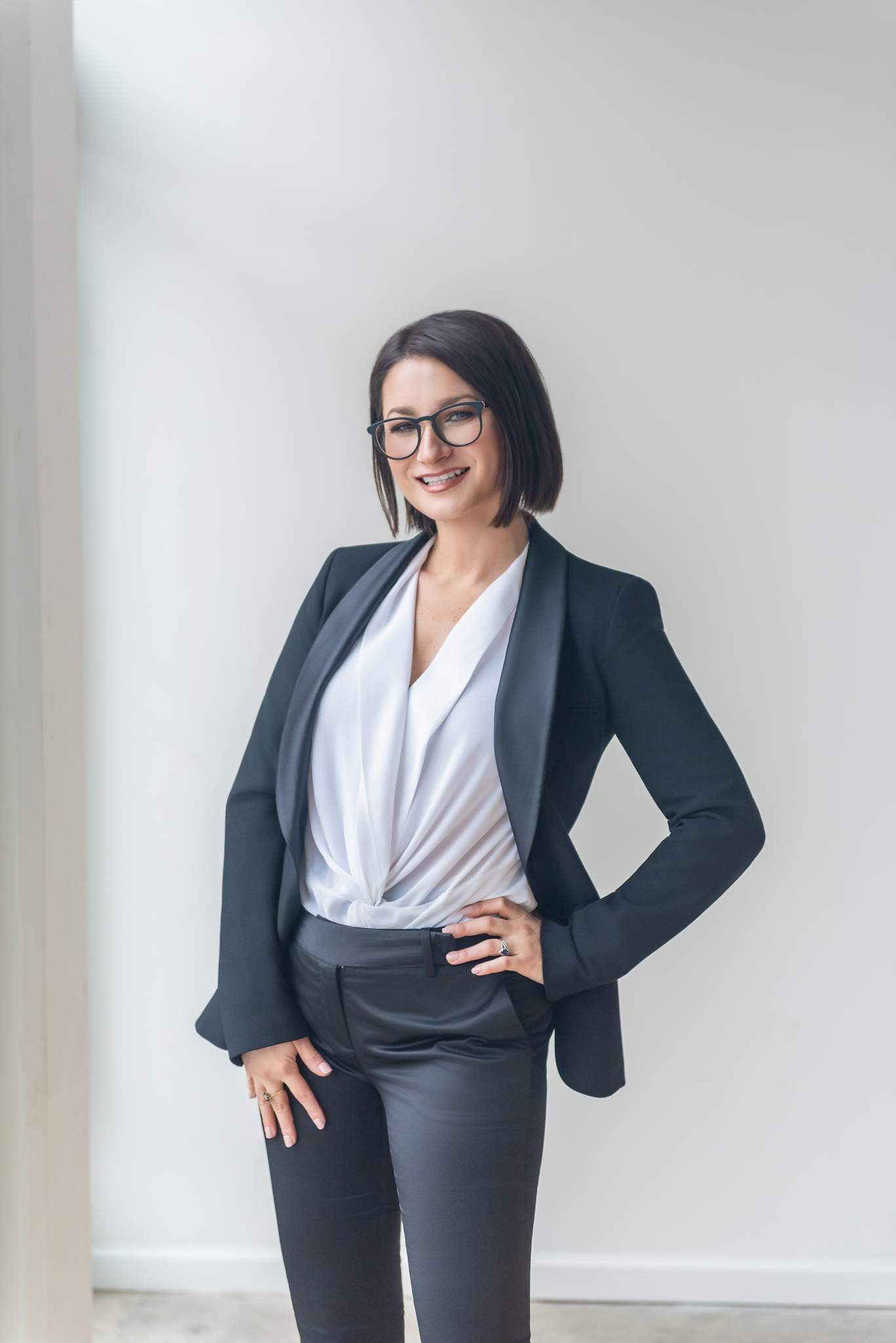 Woman with glasses in a black suit and white blouse with hands on her hips