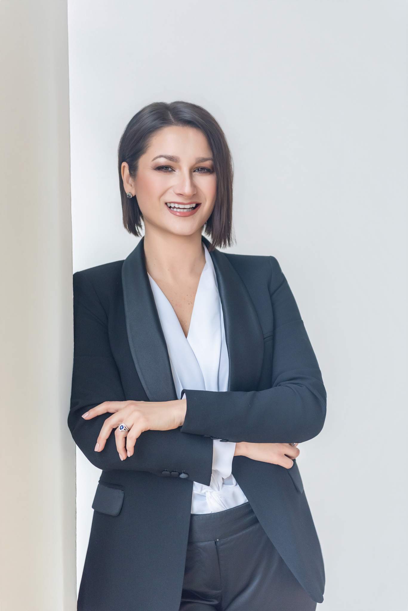 Woman in a black suit and white blouse with arms crossed in a bright studio
