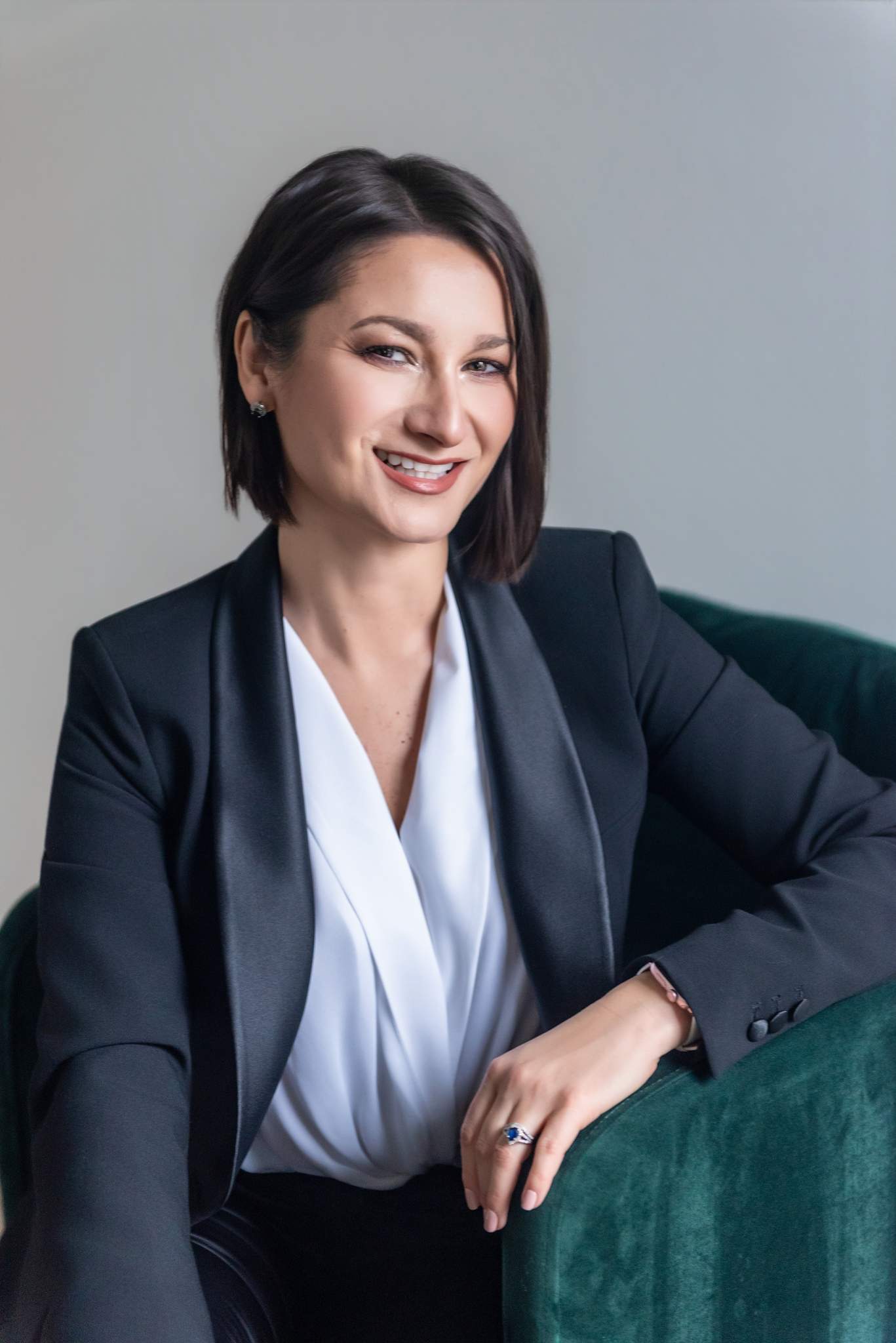 Woman in a black suit and white blouse seated in a green velvet chair
