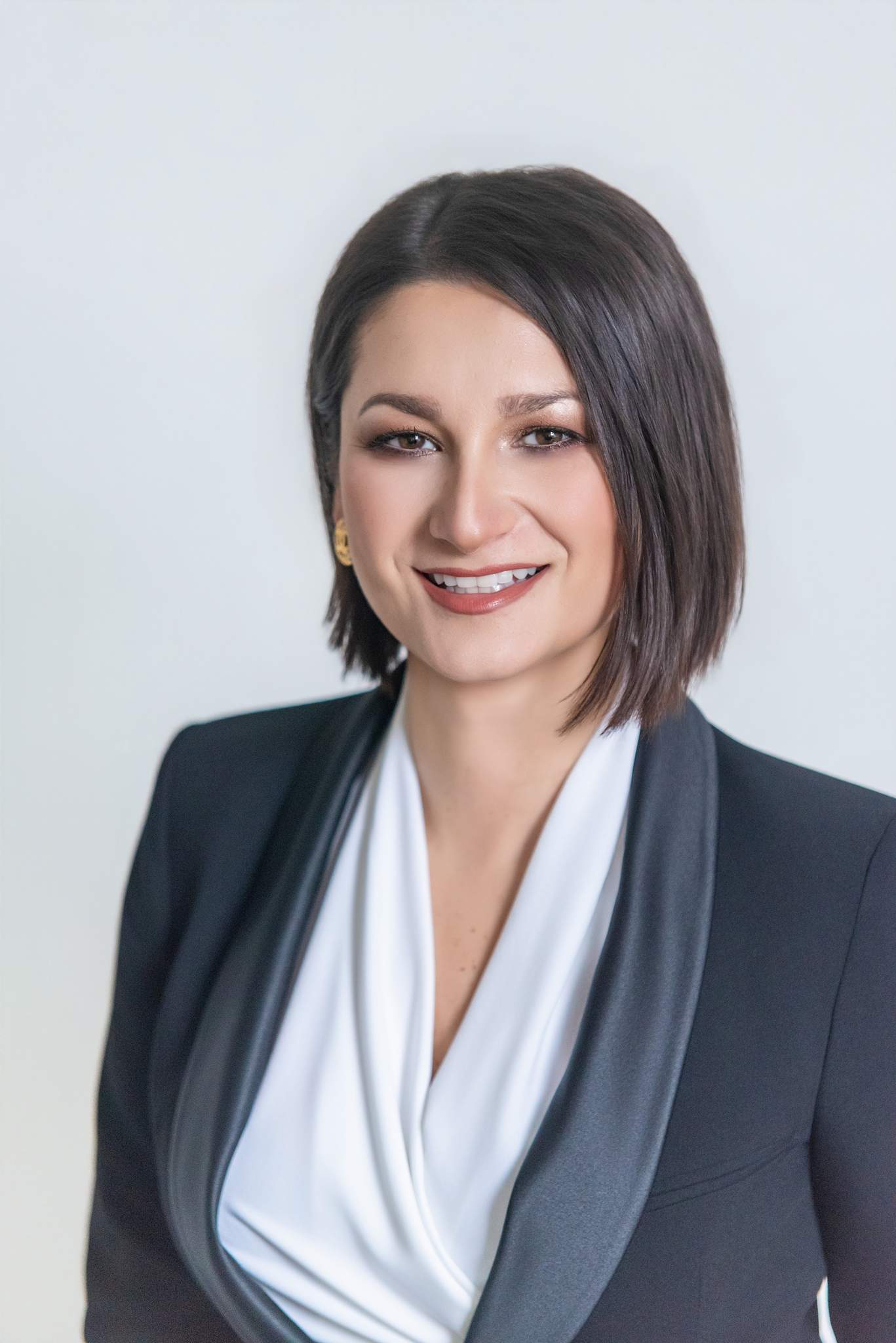 Smiling headshot of a woman in a black suit jacket with a white V-neck blouse