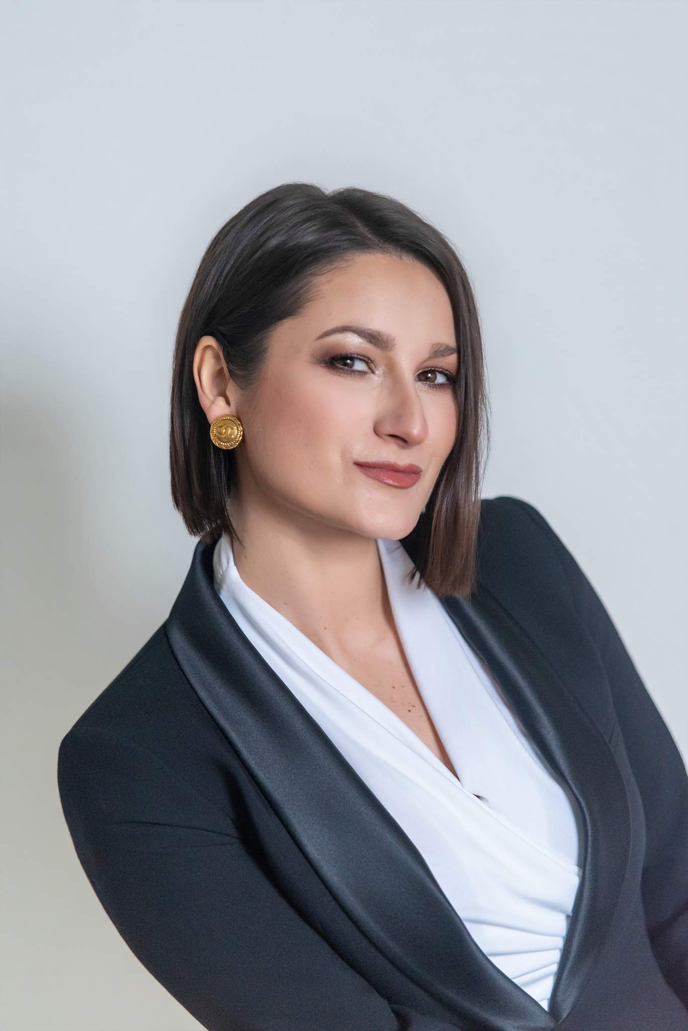 Angled headshot of a woman in a black suit jacket and white blouse with gold earrings