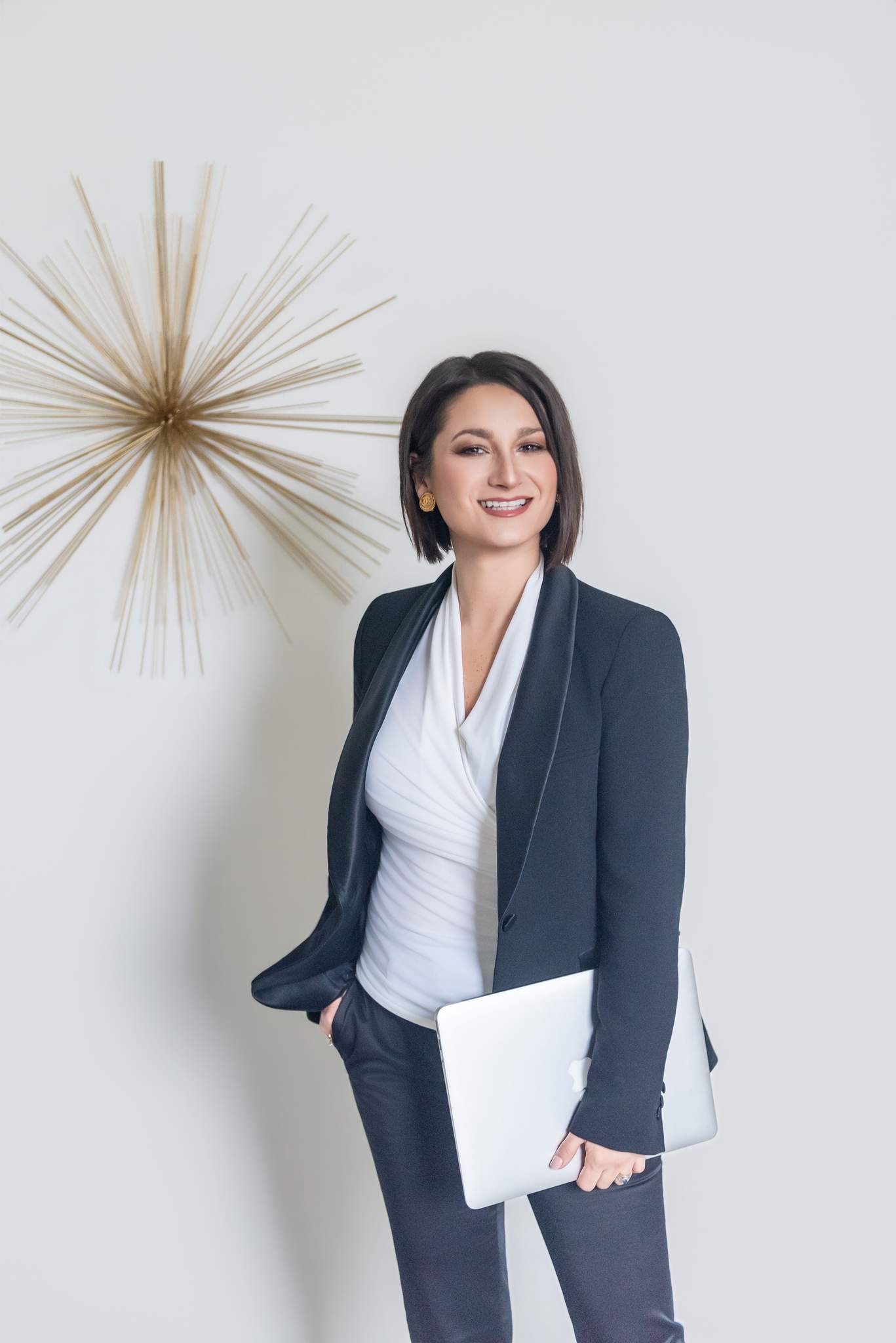 Woman in a black suit holding a laptop beside a gold starburst wall decor