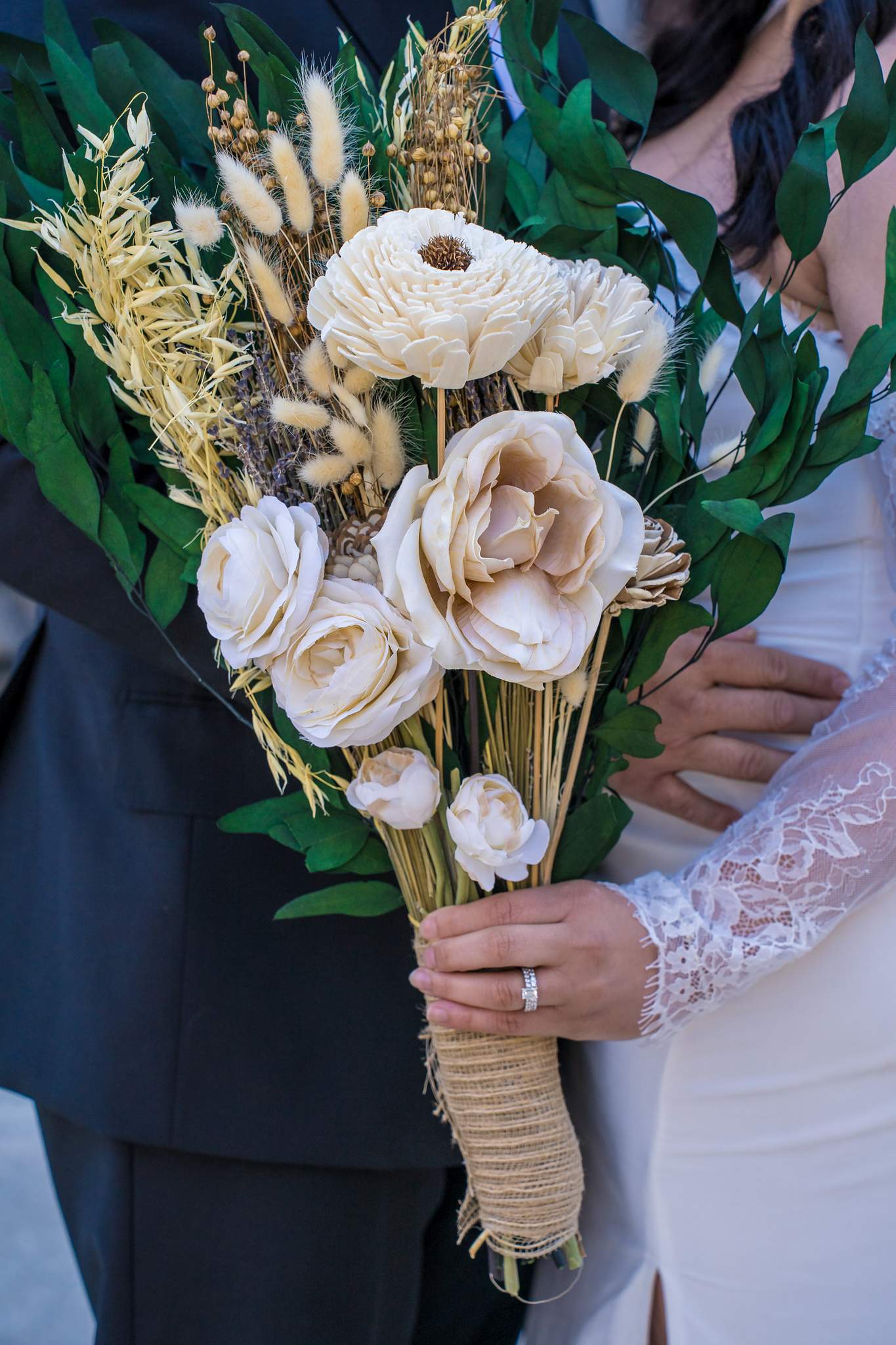 Cream wood-flower and dried grass bouquet with a jute-wrapped handle beside a lace bridal sleeve