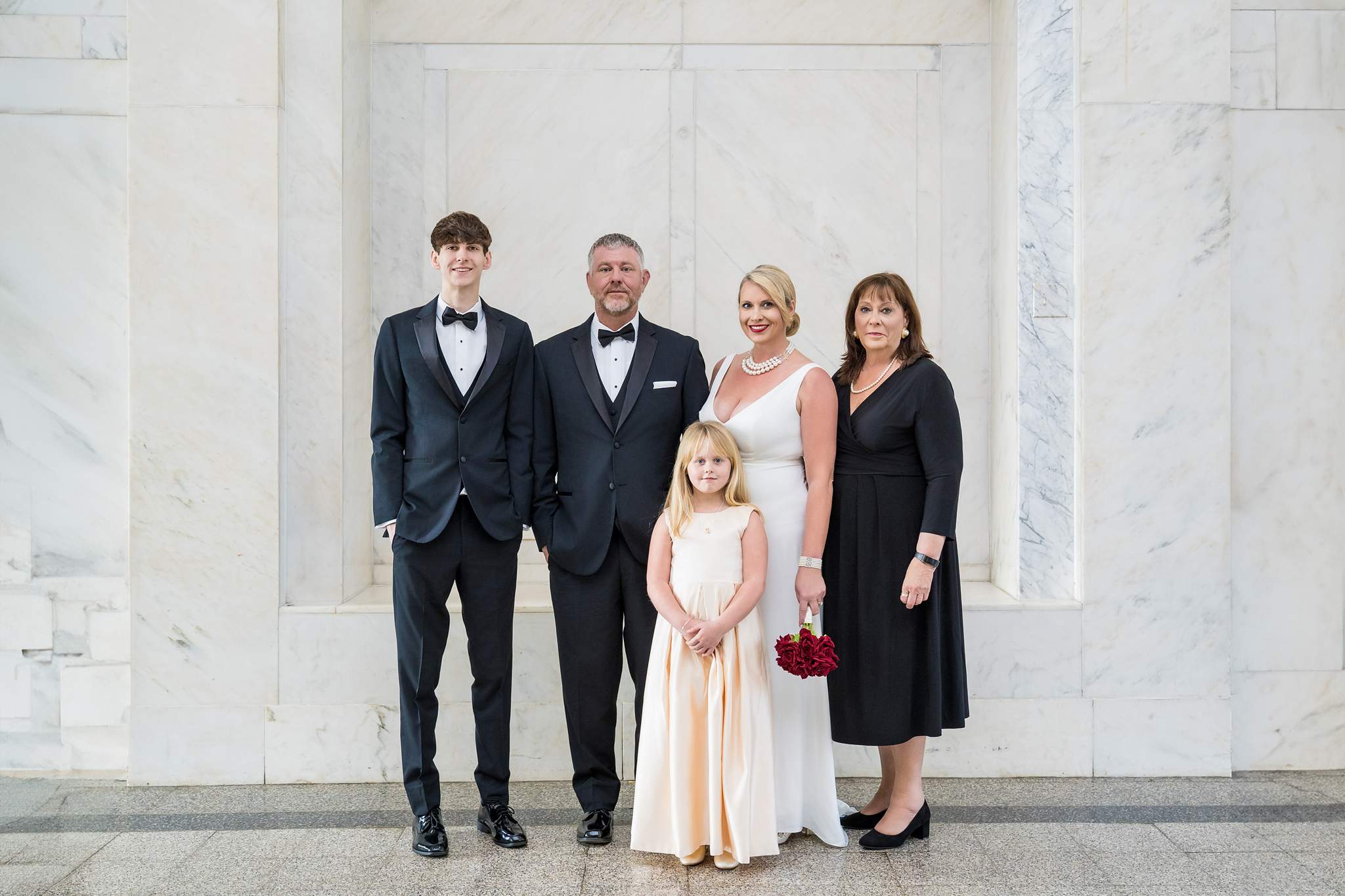 Family members in black tuxedos, a black dress and champagne satin with the couple in a marble hall