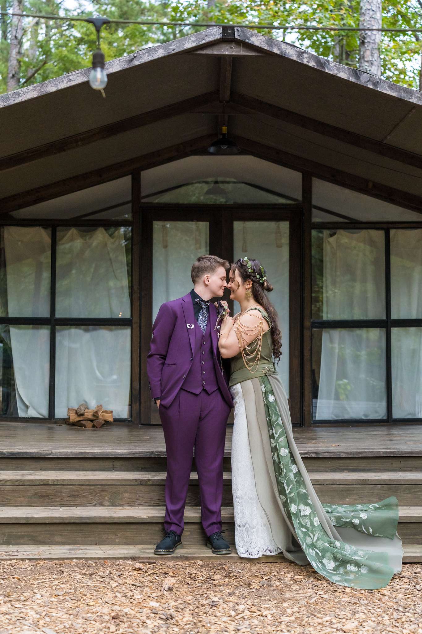 Long sage cape with floral appliques trailing down rustic cabin steps as the couple shares a kiss