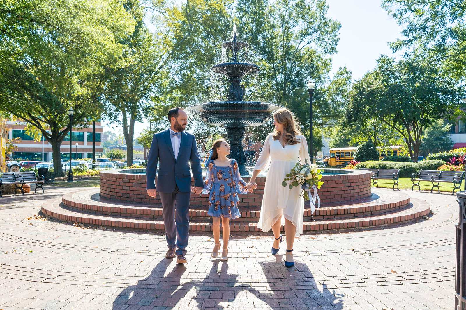 Blue suit, white midi dress and blue floral dress as a family walks past a town square fountain