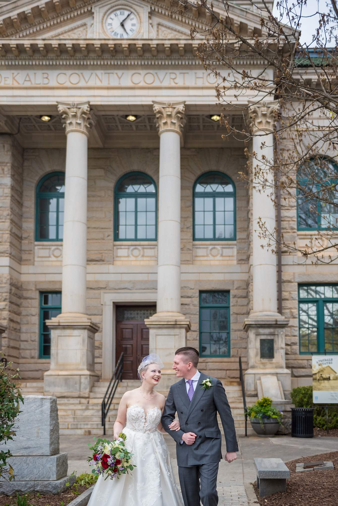 Strapless ball gown and gray suit as the couple walks outside the historic DeKalb County Courthouse