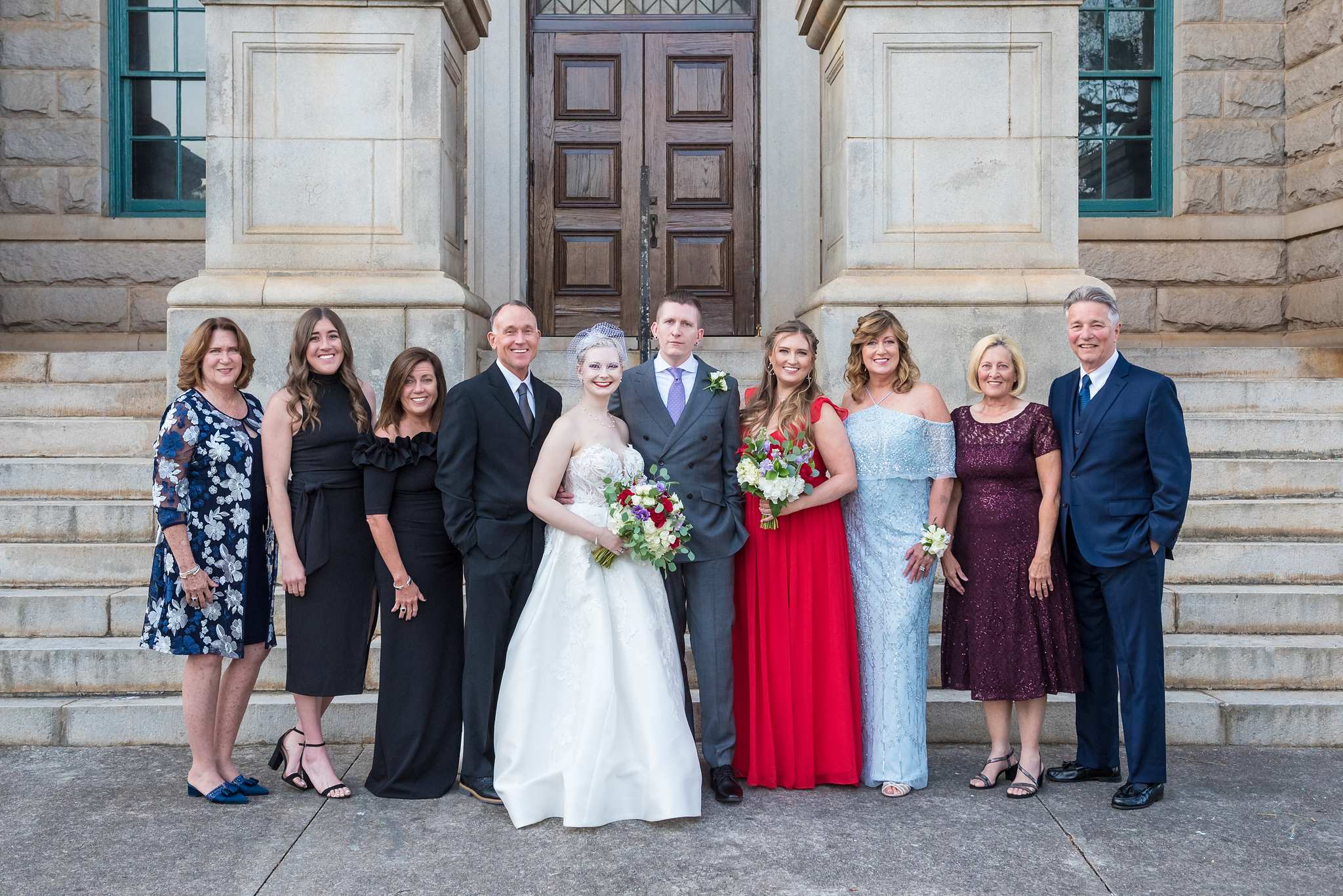 Family and guests in navy florals, black, red, light blue and burgundy beside the couple on courthouse steps